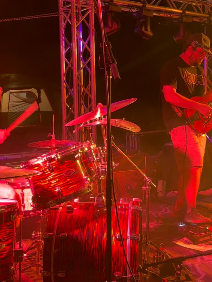 A painted figure performing on a dark, red-lit stage
